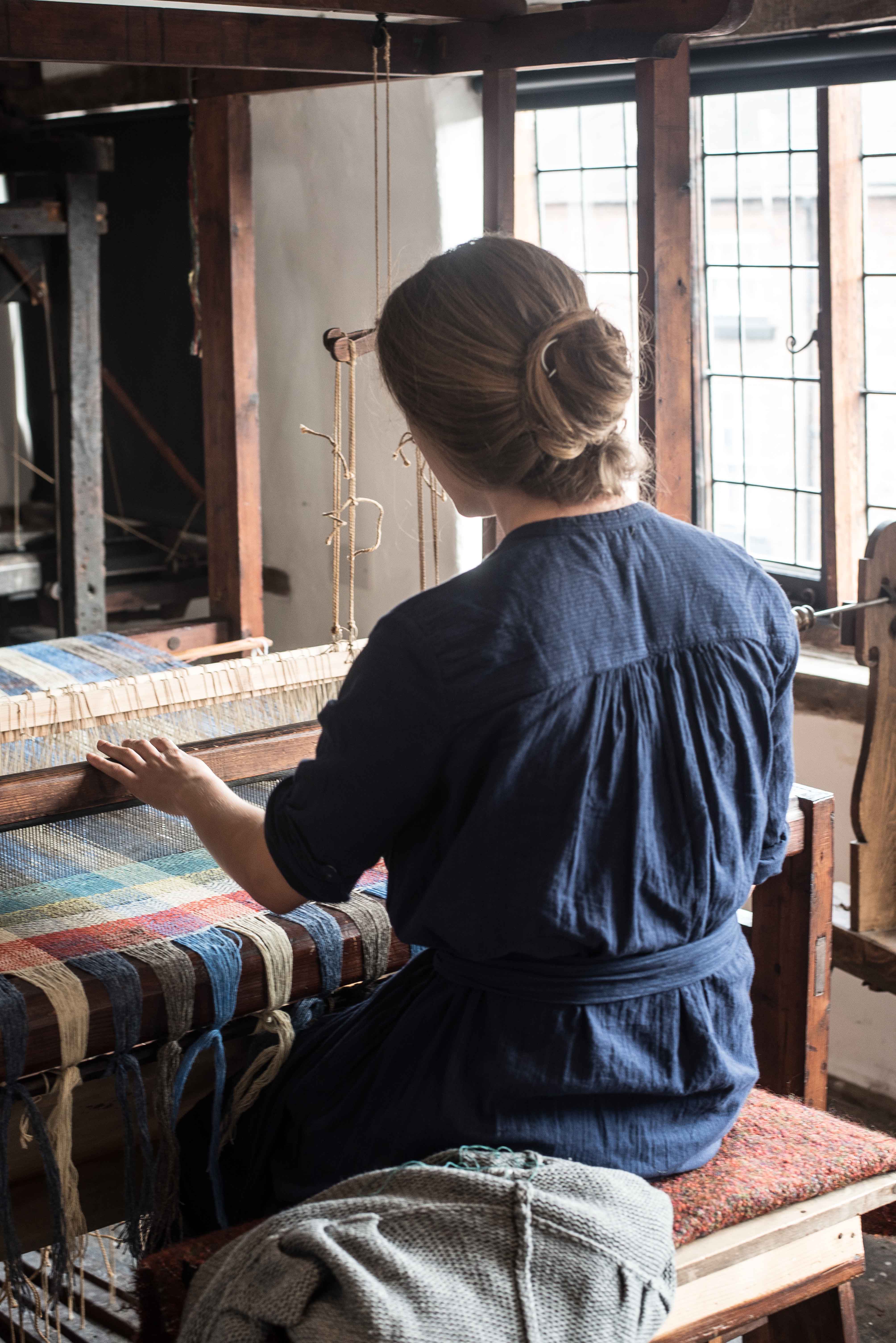 Image of a weaver sitting in front of a loon where she is weaving